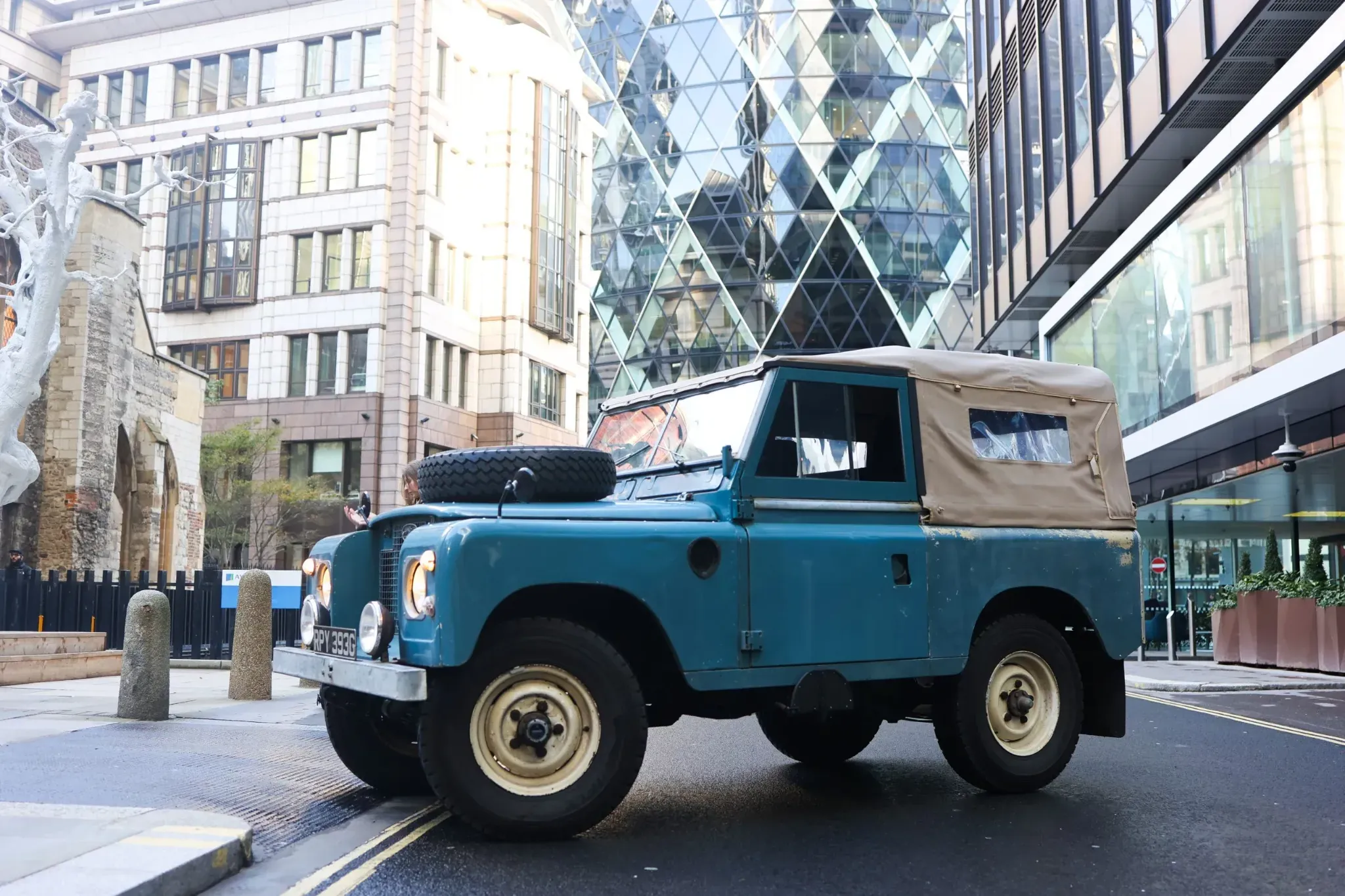 Blue Land Rover Series with beige canvas roof parked in London city street.