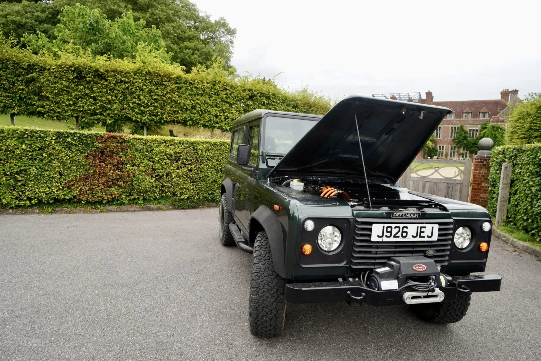 Dark green Land Rover Defender with bonnet open, showcasing its electric conversion system.