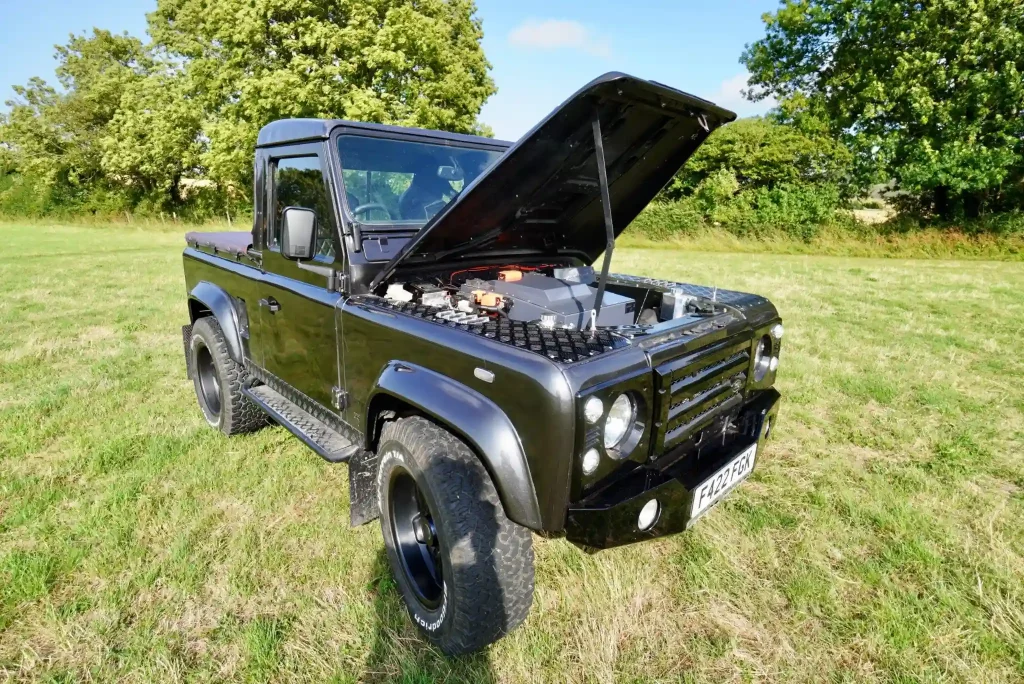 Black Land Rover Defender electric conversion parked on grass with bonnet open.
