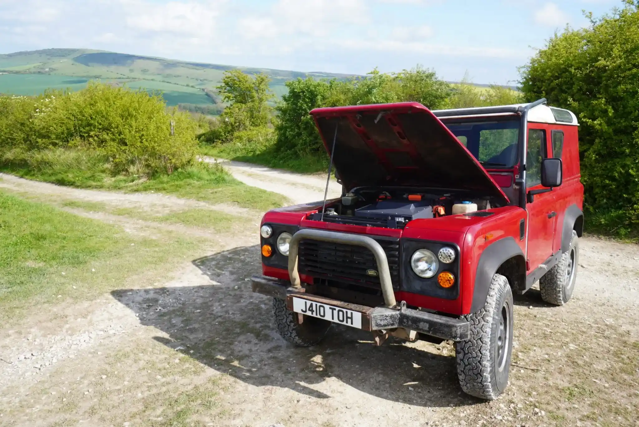 Red Land Rover Defender electric conversion parked outdoors with bonnet open.