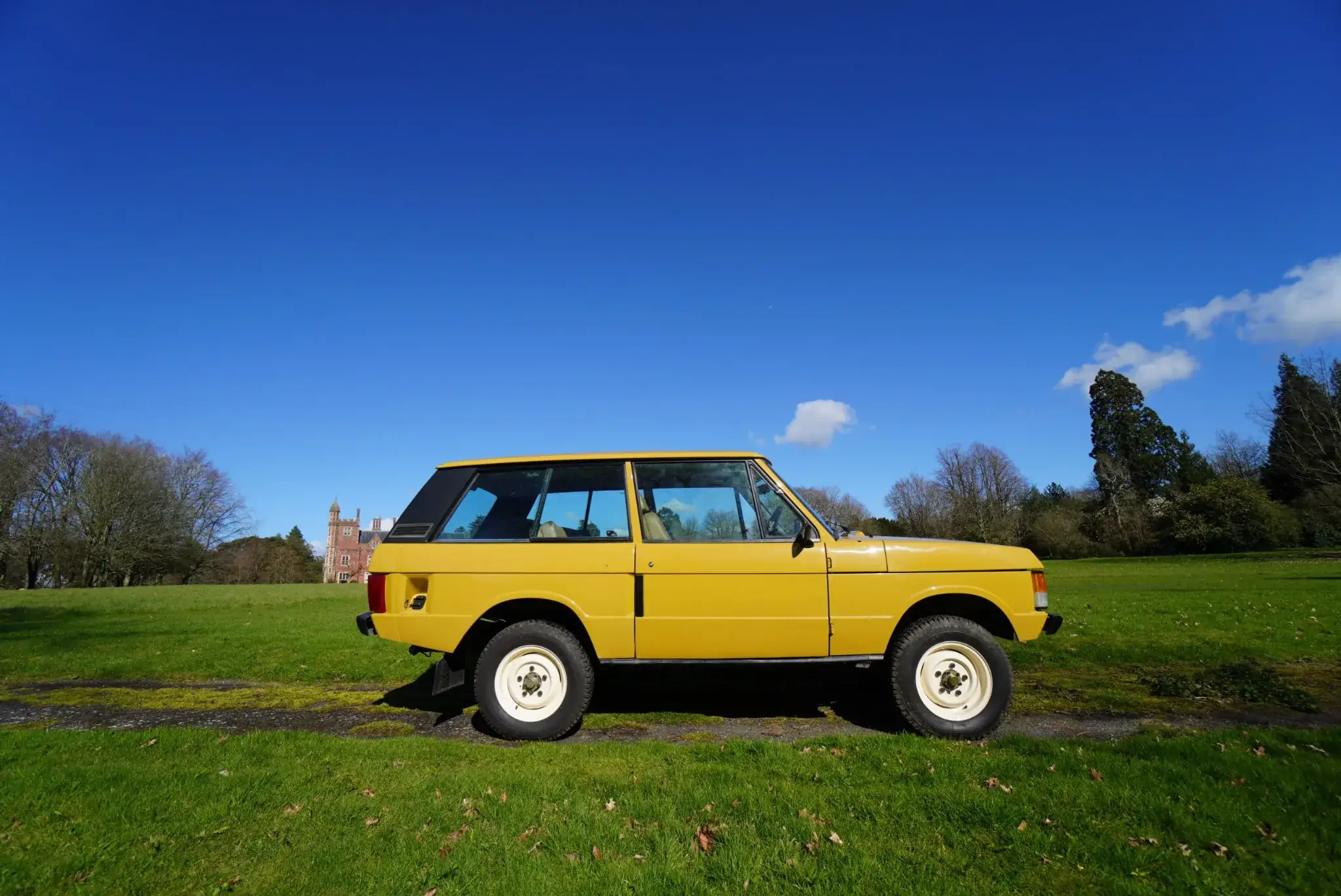 Yellow Range Rover Classic converted to electric, parked on grass under a clear blue sky.